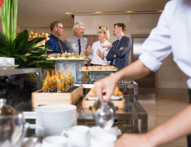 Group of four cheerful business people talking in buffet restaurant. Waitress serving coffee in frontground